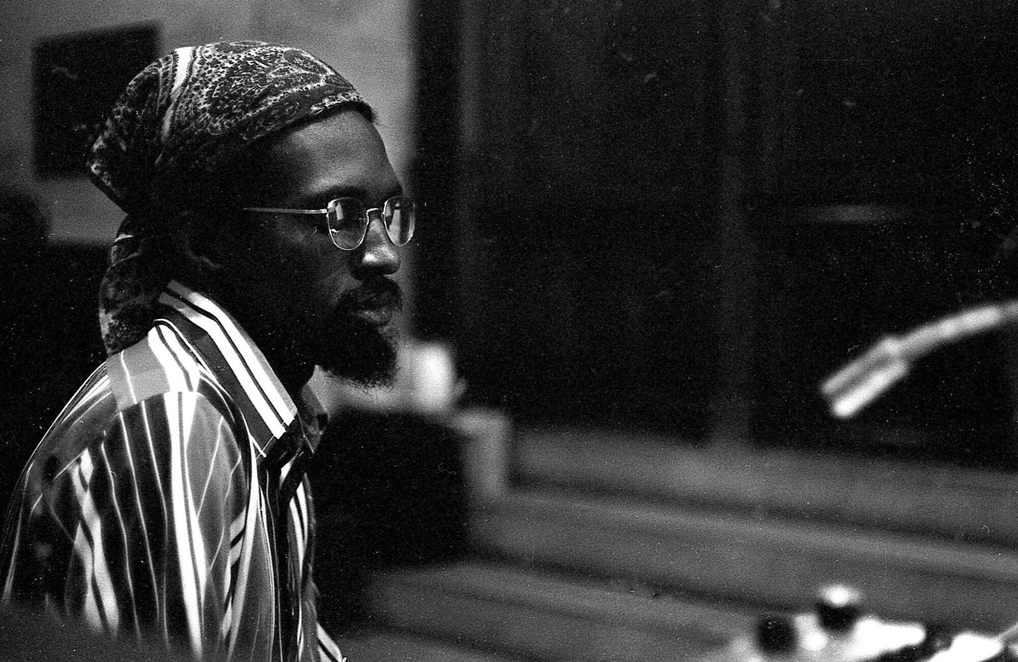 Julius Eastman in a striped shirt and bandana, in profile at a rehearsal